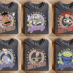 May include: Six charcoal gray t-shirts featuring Toy Story characters. Each shirt displays a circular graphic with a checkered border and stars. Characters include Mr. Potato Head, Buzz Lightyear, Jessie, Bo Peep, Woody, and an Alien with text.
