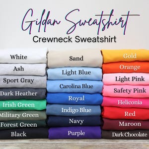 May include: A stack of Gildan crewneck sweatshirts in various colors, including white, ash, sport gray, dark heather, Irish green, military green, forest green, and black. Other colors include sand, light blue, Carolina blue, royal, indigo blue, navy, and purple.