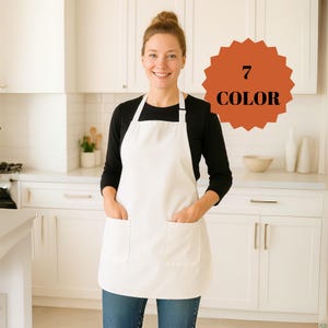 May include: A white apron with two front pockets is worn over a black long-sleeve shirt and blue jeans. The apron has a bib and a neck strap. A circular orange graphic with the text "7 COLOR" is in the background.