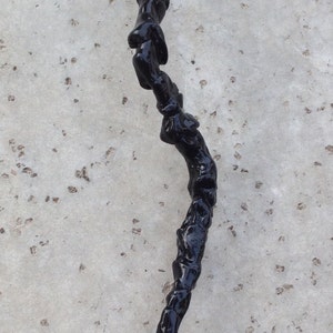 May include: A black walking stick with a twisted, gnarled design. The stick is made of wood and has a smooth, polished finish.