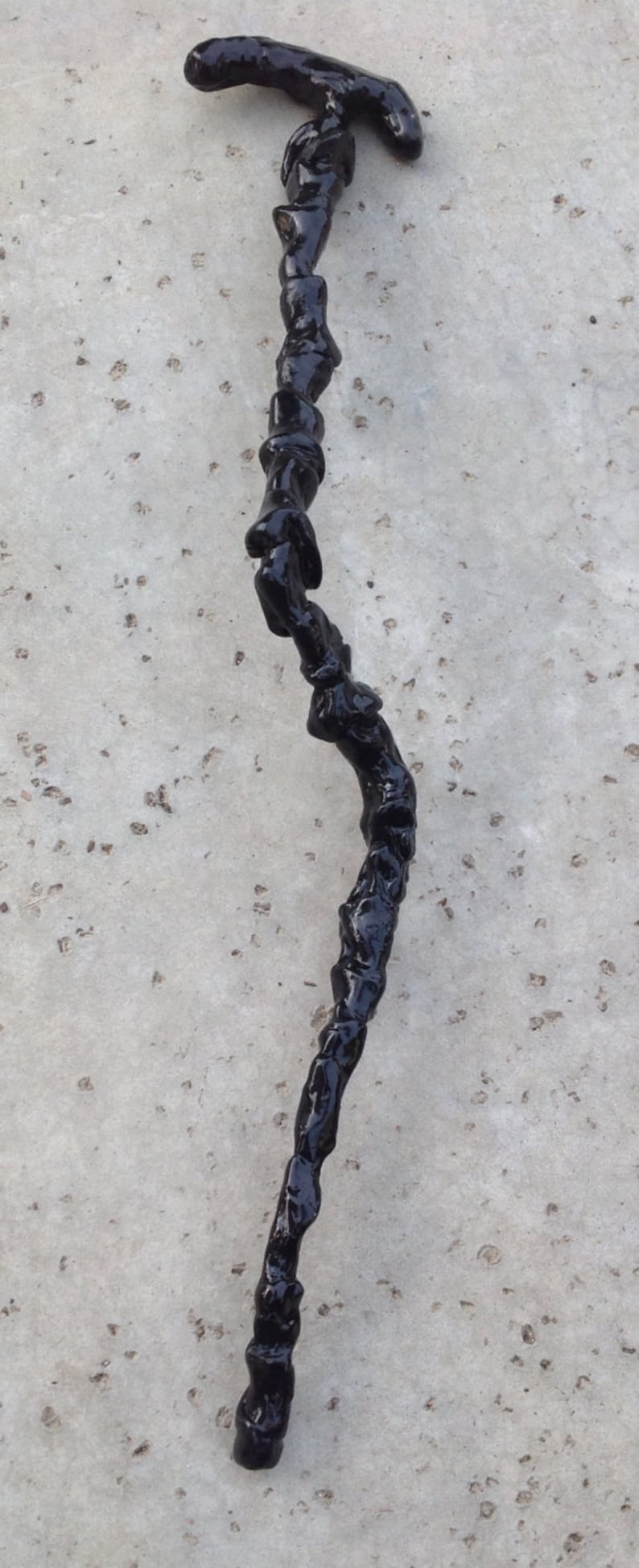 May include: A black walking stick with a twisted, gnarled design. The stick is made of wood and has a smooth, polished finish.