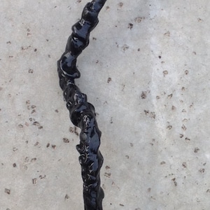 May include: A black, twisted, resin-like object on a gray, textured surface.