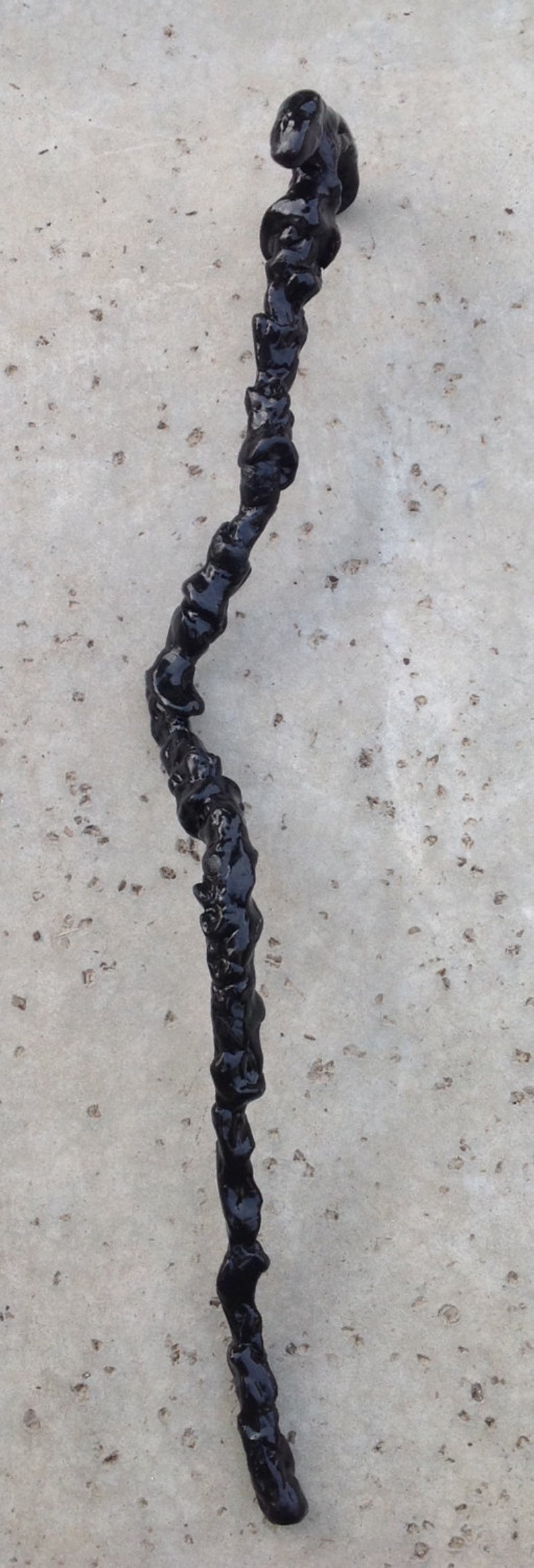 May include: A black, twisted, resin-like object on a gray, textured surface.