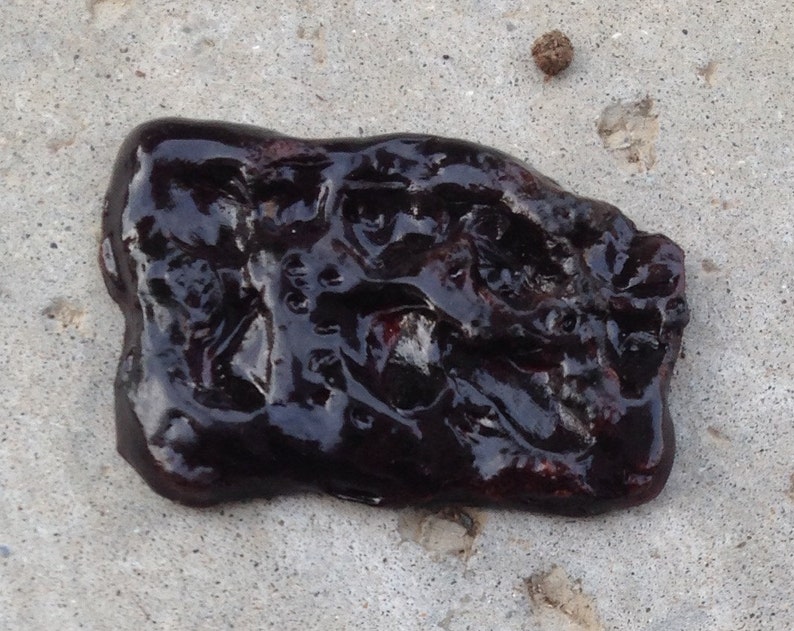 May include: A close-up of a dark, shiny, irregularly shaped object with a textured surface. The object appears to be made of a viscous substance, possibly a type of resin or tar.