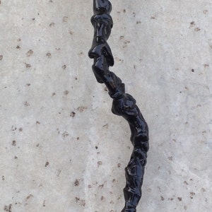 May include: A black walking stick with a curved handle. The stick is made of a material that looks like wood or plastic and has a rough texture.