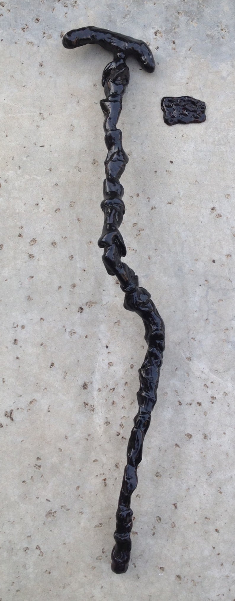May include: A black walking stick with a curved handle. The stick is made of a material that looks like wood or plastic and has a rough texture.