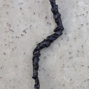May include: A black, twisted, resin stick with a rough, textured surface.