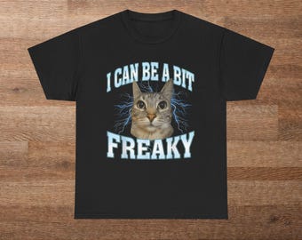 Könnte beinhalten: Schwarzes T-Shirt mit einem Katzen-Gesicht-Motiv und dem Text "I CAN BE A BIT FREAKY" in Weiß und Hellblau. Das Katzenmotiv ist zentriert und von Blitzmustern umgeben.