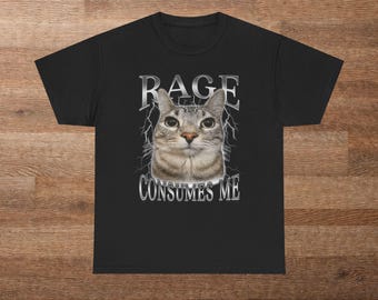 May include: Black t-shirt featuring a cat with the text "RAGE CONSUMES ME" in silver lettering. The cat has gray and brown fur and is centered on the shirt. Lightning bolt graphics are behind the cat and the text.