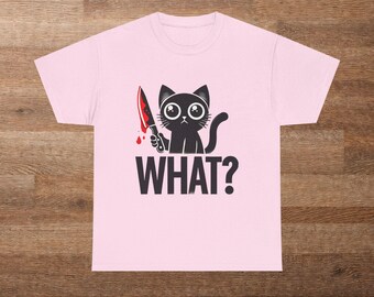 May include: A light pink t-shirt featuring a black cat holding a bloody knife. The cat has large, round eyes and a curved tail. Below the cat is the word "WHAT?" in bold, black letters.