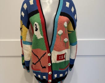 May include: A colorful, button-down cardigan sweater with a golf theme. The sweater features a variety of colors and patterns, including golf balls, golf clubs, and the number "18" on a flag. The sweater has a V-neck and long sleeves.