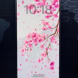 May include: A smartphone displays a floral wallpaper featuring pink cherry blossoms and falling petals against a light gray background. The time, 10:18, and date, Fri Oct 24, are visible. The phone shows 5 notifications.