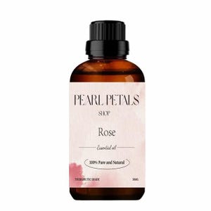 May include: A brown glass bottle of rose essential oil with a black cap. The label reads "Pearl Petals Shop Rose Essential Oil 100% Pure and Natural Therapeutic Grade" with a pink watercolor accent. The bottle contains 50ml of oil.