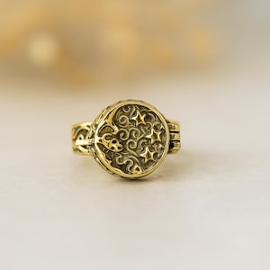 Könnte beinhalten: Ein goldfarbener Ring mit einem Himmelsdesign. Der Ring hat eine runde Oberfläche mit einem Mond und Sternen, umgeben von Wirbelmustern. Das Band hat aufwendige Details. Ein einzigartiges Schmuckstück.