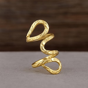Op de afbeelding: Een goudkleurige ring met een open, wervelend ontwerp. De ring heeft een reliëfpatroon en een gepolijste afwerking. Het ontwerp wikkelt zich om de vinger en creëert een unieke uitstraling. De ring is waarschijnlijk gemaakt van metaal.