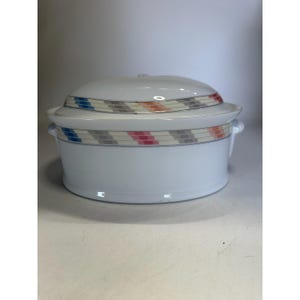 May include: White ceramic casserole dish with a lid. The dish has a geometric pattern of blue, gray, pink, and orange rectangles around the rim. It has two small handles on the sides and a small knob on the lid.