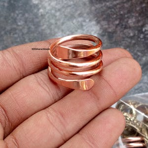 Op de afbeelding: Een koperkleurige spiraalring. De ring wikkelt zich meerdere keren om de vinger, waardoor een gelaagd effect ontstaat. Het metaal heeft een gepolijste afwerking, die licht reflecteert. De ring is een sieraad.