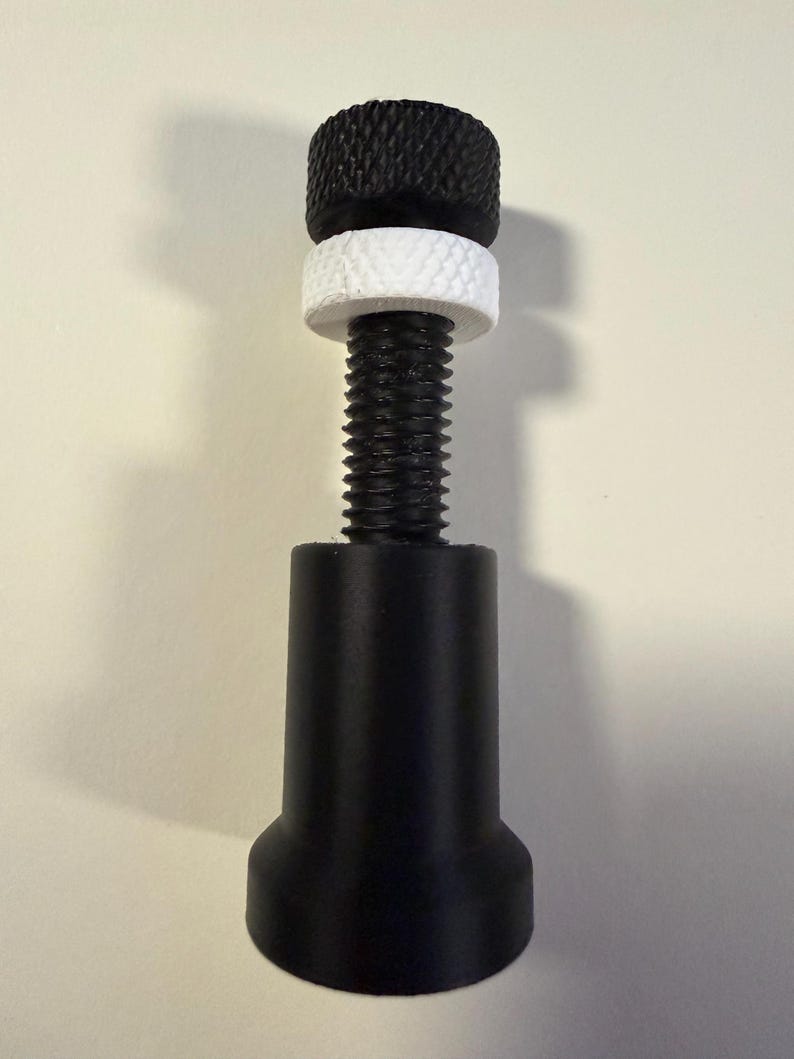 Op de afbeelding: Een zwarte verstelbare meubelpoot met een zwarte knop met textuur, een witte ring en een schroefdraad. De basis van de poot is ook zwart. Dit product is ontworpen voor meubelondersteuning en -nivellering.