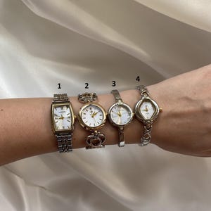 Puede incluir: Se muestran cuatro relojes de pulsera vintage en tonos dorados y plateados. Los relojes tienen varias formas de esfera, incluyendo rectangular, redonda y ovalada. Las correas de los relojes son de metal y tienen diferentes diseños. Los relojes están en la muñeca de una persona.