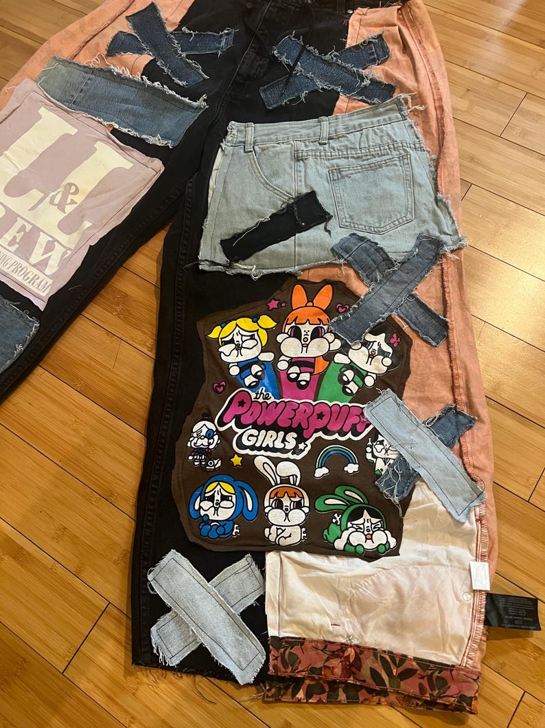 May include: A patchwork design featuring denim shorts, a pink t-shirt with text, and a brown patch with Powerpuff Girls characters. Denim patches are sewn onto black and pink fabric.