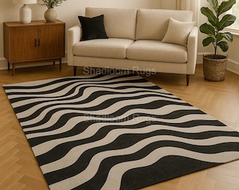 May include: A large, rectangular rug with a wavy pattern of black and beige stripes. The rug is placed on a hardwood floor in a living room setting, with a sofa, side table, and decorative items in the background. The rug's design adds a modern touch to the room.