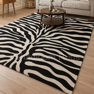 Könnte beinhalten: Ein rechteckiger Teppich mit einem auffälligen Zebramuster in Schwarz und Off-White. Der Teppich liegt auf einem Holzboden in einem Wohnzimmer, mit einem Sofa und einem Couchtisch im Hintergrund. Der Teppich setzt einen auffälligen Kontrast zur Einrichtung des Raumes.
