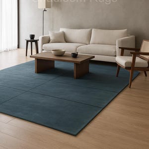 Peut inclure: Salon moderne avec un grand tapis rectangulaire bleu sarcelle. Un canapé clair, une table basse en bois et une chaise avec un dossier en osier sont disposés sur le tapis. Le mur est de couleur neutre et le sol est en bois.