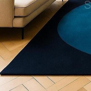 May include: A navy blue and teal geometric rug with a modern design. The rug features a large teal circle and a triangular shape, creating a contemporary aesthetic. The rug is placed on a wooden floor, with a portion of a beige sofa visible.