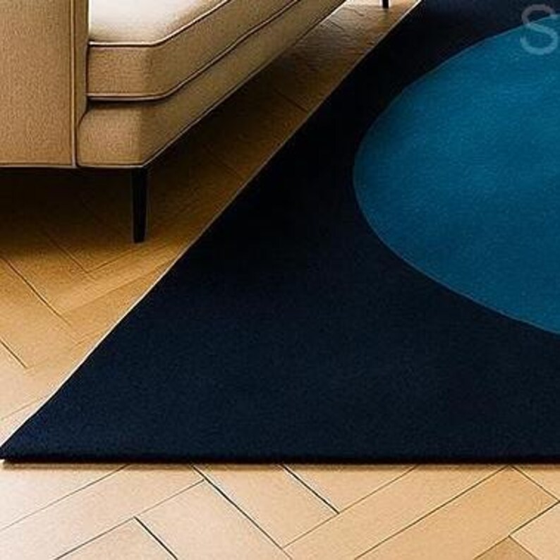 May include: A navy blue and teal geometric rug with a modern design. The rug features a large teal circle and a triangular shape, creating a contemporary aesthetic. The rug is placed on a wooden floor, with a portion of a beige sofa visible.