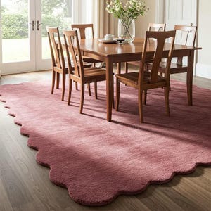 Pode incluir: Uma sala de jantar com uma mesa e cadeiras de madeira, sobre um grande tapete rosa empoeirado com borda ondulada. Um vaso de flores está sobre a mesa. A sala tem luz natural.