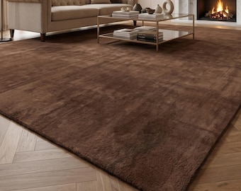 May include: A large, rectangular area rug in a solid, deep chocolate brown color with a soft, plush texture. The rug features a uniform, dense pile that covers the floor, extending from the foreground toward the center of the room.