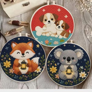 May include: Three embroidered hoops featuring cute animal designs. One shows two puppies with a bone on a red background. Another depicts a fox holding a lantern. The last one shows a koala with a lantern.