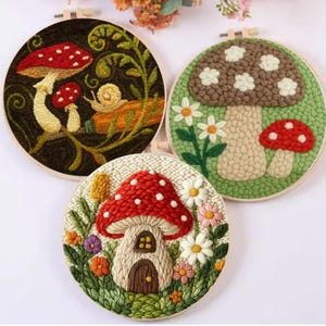 May include: Three round embroidery hoops featuring mushroom designs. One has a red mushroom with white spots and a snail. Another has a brown mushroom with white spots and daisies. The third has a red mushroom house with flowers.