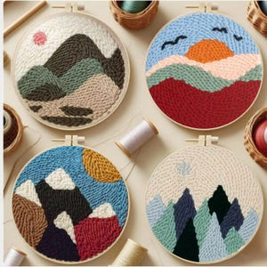 May include: Four round embroidery hoops with landscape designs. Each features a different mountain scene in various colors, including blue, green, brown, and red. The designs are created with textured yarn, and the hoops are displayed with spools of thread.