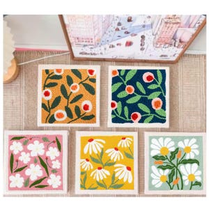 May include: Five square floral art pieces with white borders. The designs feature various flowers and foliage in shades of yellow, pink, blue, and green. The artwork is displayed on a neutral-toned surface.