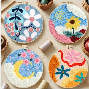 May include: Four round embroidery hoops with floral and celestial designs. The hoops feature a variety of colors, including blue, pink, yellow, and orange. Each design is set in a wooden hoop, showcasing a handmade craft.