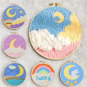 May include: A collection of handmade embroidery hoops featuring celestial designs. Each hoop showcases a crescent moon, clouds, and stars in various color palettes, including blue, yellow, pink, and purple. One hoop has the word "lucky" embroidered.