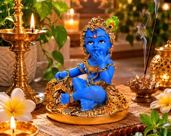 May include: A blue-skinned figurine of a child deity sitting in a cross-legged position, adorned with gold-colored jewelry and a peacock feather. The figure is surrounded by brass oil lamps, white flowers, incense smoke, and prayer beads.