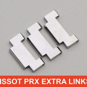 May include: Three silver-toned watch links, designed for a Tissot PRX watch, are arranged on a light gray surface. Each link has a rectangular center with a T-shaped end. The text "TISSOT PRX EXTRA LINKS" is displayed in a red banner.