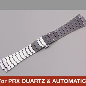 May include: A silver-toned watch band with a rectangular link design. The band is made of metal and has a clasp in the center. The text "For PRX QUARTZ & AUTOMATIC" is displayed at the bottom.