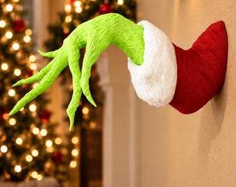 May include: A wall-mounted decorative sculpture featuring a long, textured, bright green hand with slender fingers extending from a red sleeve cuff trimmed with a thick, white, fuzzy material, designed to look like a character arm.