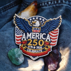 Puede incluir: Parche bordado con el texto "AMERICA 250" y las fechas "1776-2026" que celebra el 250 aniversario. El parche presenta un águila calva, elementos de la bandera estadounidense y la palabra "CELEBRATE". El parche está sobre un fondo de mezclilla.