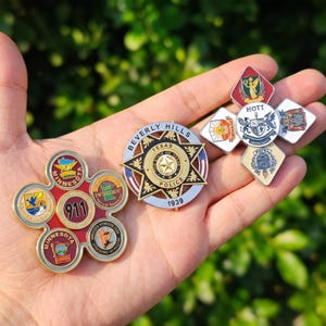 Peut inclure: Une collection de badges et d'épingles de la police et des services d'urgence. Les badges présentent divers motifs, dont un badge en forme d'étoile avec "Beverly Hills Texas Police 1939" et une épingle en forme de fleur avec "Minnesota 911".