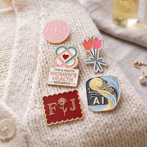 May include: Five enamel pins featuring diverse designs: a pink circular pin with a passport icon, a bouquet of three tulips, a heart-shaped emblem with the text CARE & HEALTH WOMEN'S HEALTH RESEARCH, a red scalloped square with the letters F J and a rose, and a blue pin with the text AI.