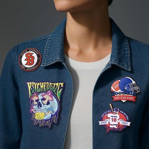 May include: A denim jacket with several patches. Patches include a baseball logo, a skull with mushrooms, a football helmet, and a patch with the number 10. The jacket is blue and has a white t-shirt underneath.