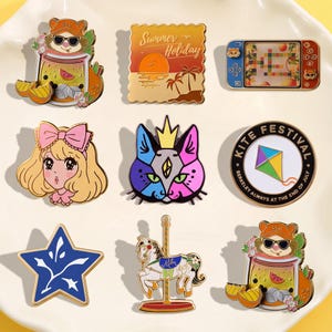 Op de afbeelding: Een verzameling kleurrijke emaille pins met diverse ontwerpen. Inclusief een hamster in een drankje, een zonsondergangscène, een videogame, een meisje met een strik, een kattenkop, een vliegerfestivalbadge, een ster en een carrouselpaard.