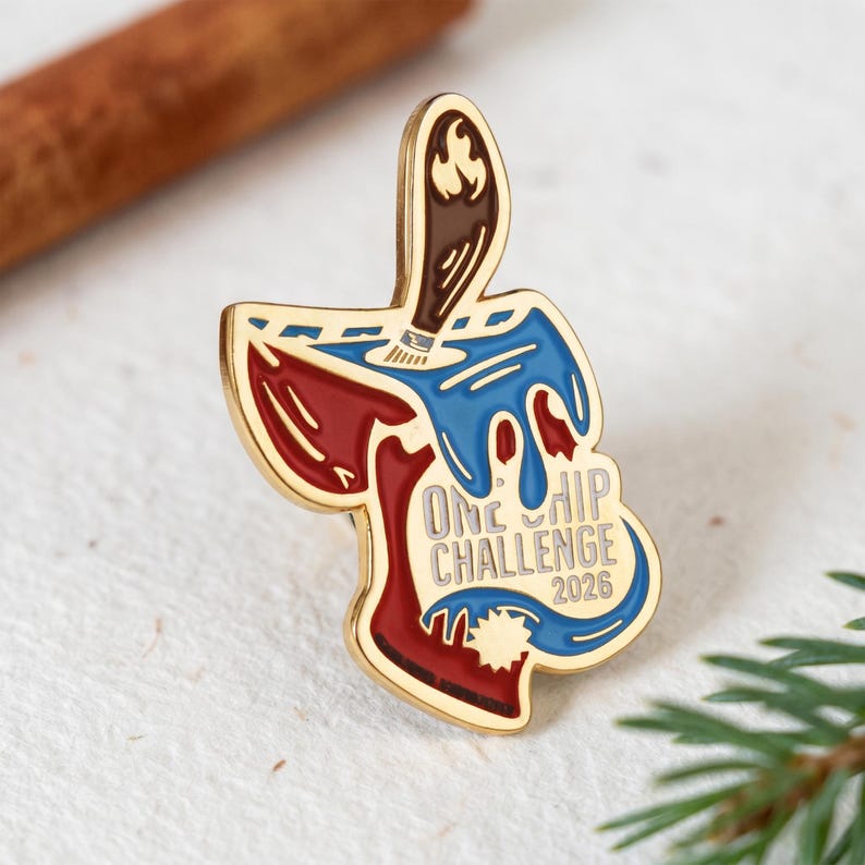 May include: A gold-toned metal enamel pin shaped like a tortilla chip dipped in blue sauce, featuring a brown paintbrush handle at the top. The text ONE CHIP CHALLENGE 2026 is printed in gray on the chip, which has a red base and blue drips.