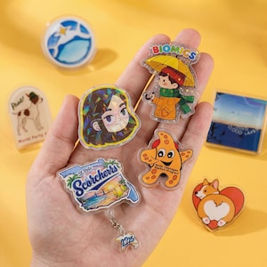 Può includere: Una collezione di spille e badge in acrilico colorati. I disegni includono un personaggio dei cartoni animati con un ombrello, una stella marina, un corgi, un ritratto e una scena sulla spiaggia di St. Pete. Altre spille raffigurano un cane e un paesaggio.