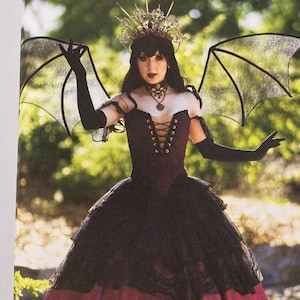 May include: A Simplicity Costumes sewing pattern envelope R12203 featuring a dark maroon and black gown with a corset-style bodice, lace-up front, layered tulle skirt, black bat-like wings, and a crown. Includes back view with corset lacing.