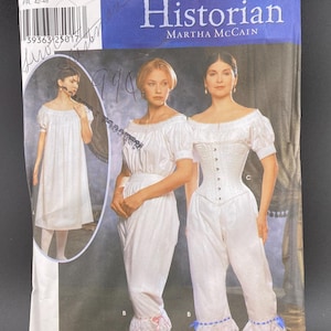 May include: Simplicity sewing pattern titled "The Fashion Historian" by Martha McCain. The pattern features illustrations of women's historical clothing, including a dress, corset, and bloomers. The pattern size is RR 14, 16, 18, and 20.